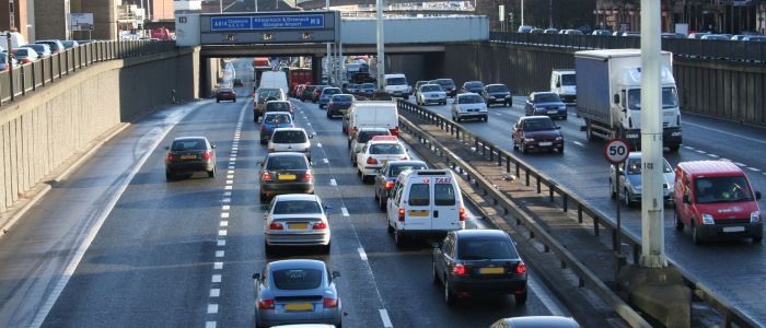 Cars going in both directions on a motorway with tall sides and signs overhead