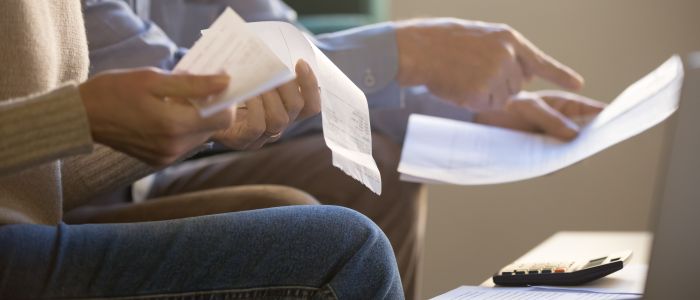 Two people's hands holding bills with a calculator on the table