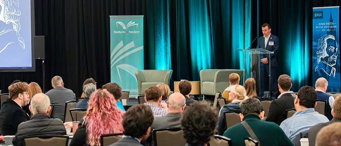 Craig Smith standing at a podium speaking to an audience. Beside him is an Adam Smith banner behind him Source: Amy Laux