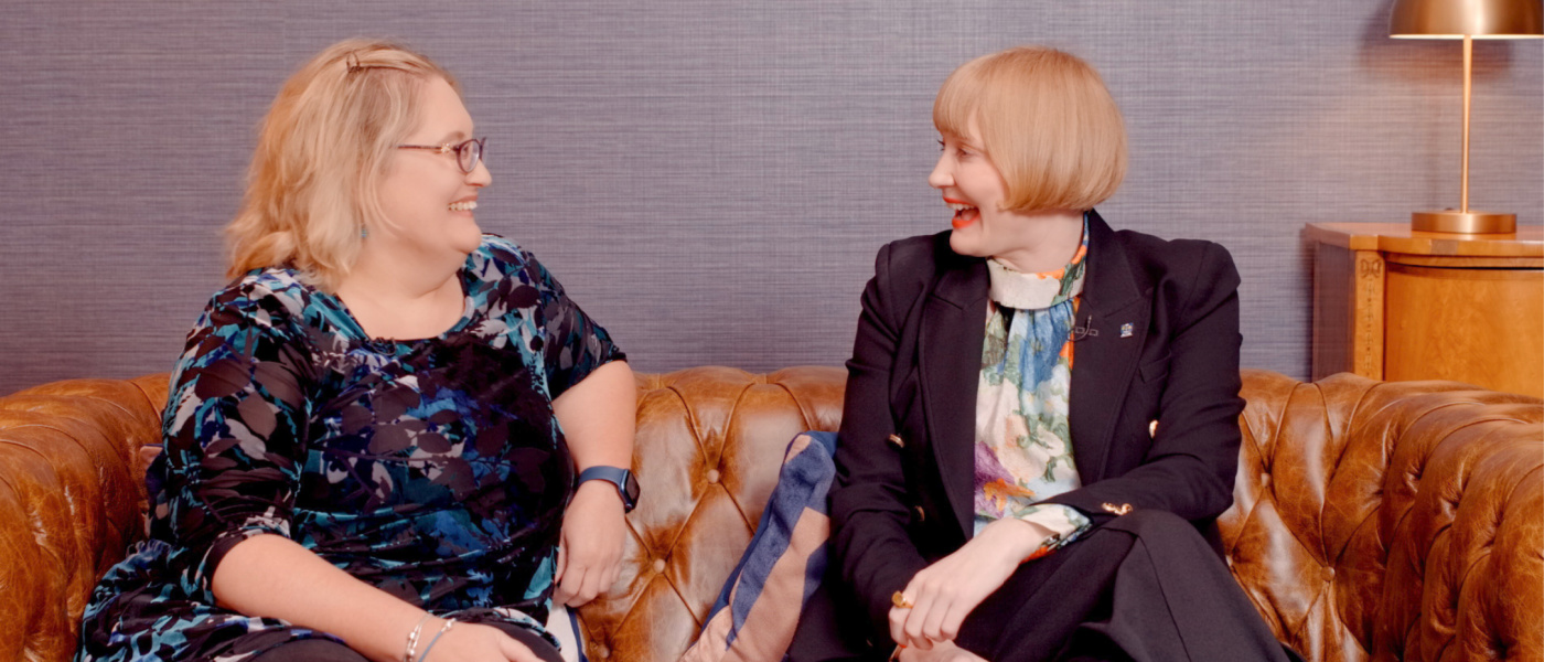 Professor Kathy Belov and Professor Rachel Sandison sat conversing together on a sofa, smiling at one another