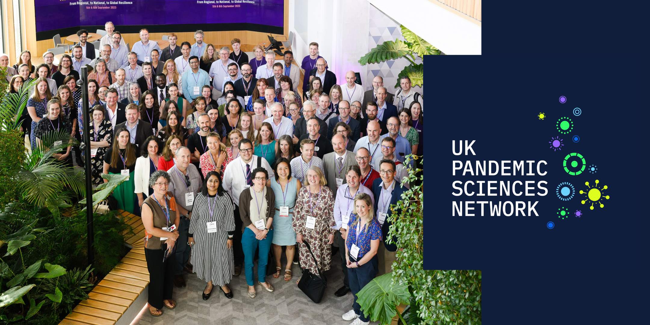 This image shows a large group of people gathered for an event, representing the UK Pandemic Sciences Network. The right side features the network's logo, with colourful virus-inspired designs.