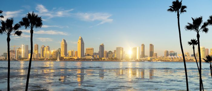 Skyline of San Diego from across the water with the sun setting between the buildings