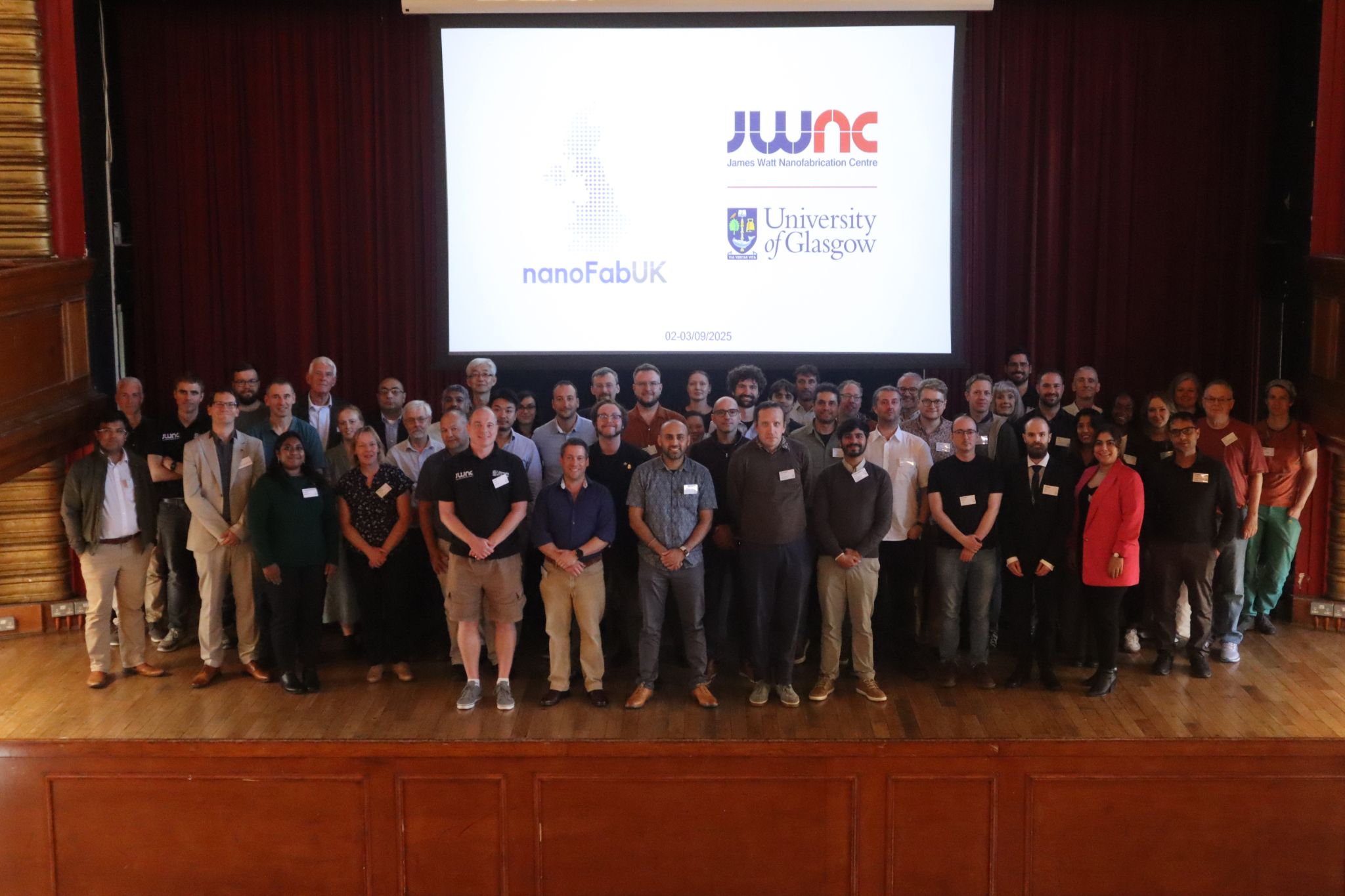 Attendees of nanoFabUK 2025 standing on the stage at the Glasgow University Union Debates Chamber