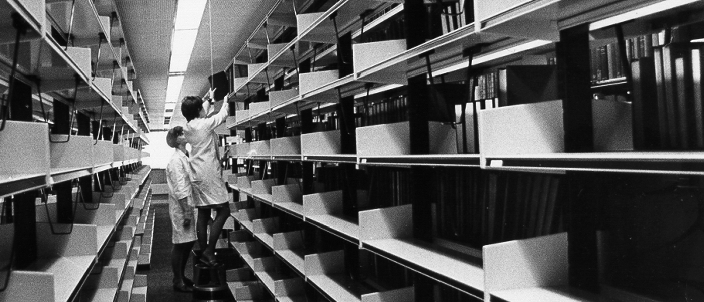 Old photo of staff stacking books on shelves in the University Library
