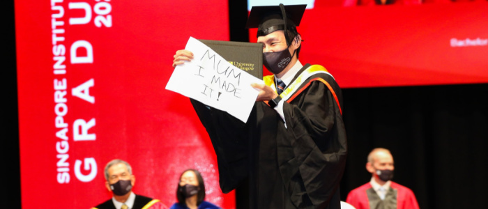 Singapore Institute of Technology graduate on the stage holding a sig saying
