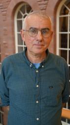 A man with glasses standing in front of brick wall with windows