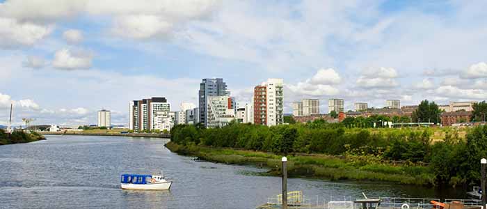 A series of flats on Glasgow's harbour with a small park in front next to a river with a small boat on the river. Source: Vetas | iStockphoto https://www.istockphoto.com/photo/passenger-ferry-sailing-from-govan-to-the-ferry-terminal-gm508125903-45512622