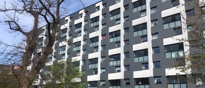 Large block of modern flats with gray and white patterned cladding and trees and gardens in front. Source: felibrilu | Flickr No credit required
