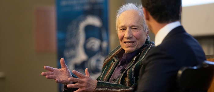 Close-up on Sam Peltzman's animated face and raised hands while he is speaking to a person whose face can't be seen. Source: Chicago Booth University