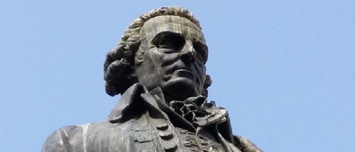 Looking up at the head of a grey statue of Adam Smith against a light blue sky. Source: Free to use under the Pixabay license No attribution required https://pixabay.com/photos/adam-smith-edinburgh-statue-4637193/