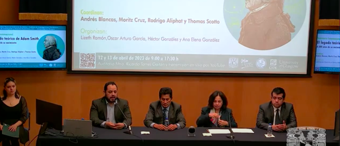 Four people sitting at a table taking part in a seminar with a screen behind them