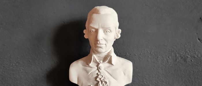A white bust of Adam Smith casting a shadow against a black background