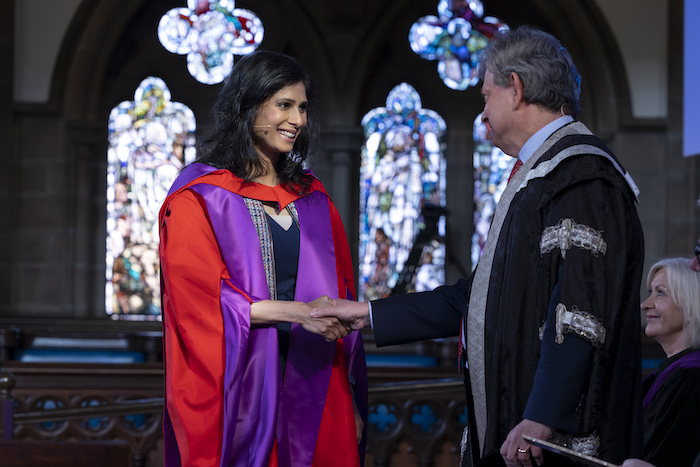 Gita Gopinath, dressed in purple and red academic robes, smiles as she shakes hands with Glasgow University principal Anton Muscatelli 