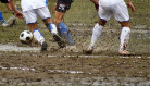 The image depicts mens legs playing football, lots of mud is splashing everywhere. They are wearing football shorts and shoes. 